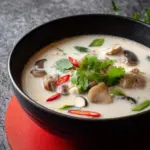 Bowl of authentic Tom Kha Gai, Thai coconut chicken soup with fresh herbs.