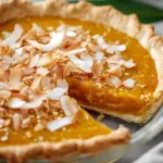Slice of Thai Coconut Pumpkin Pie topped with coconut flakes and spices